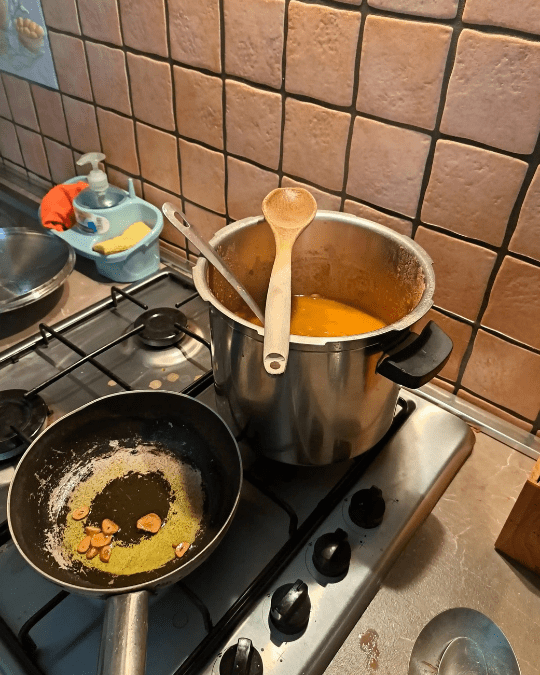 Pentola in acciaio su piano cottura con pasta e fagioli cremosa e padellino con aglio soffritto in olio d'oliva.